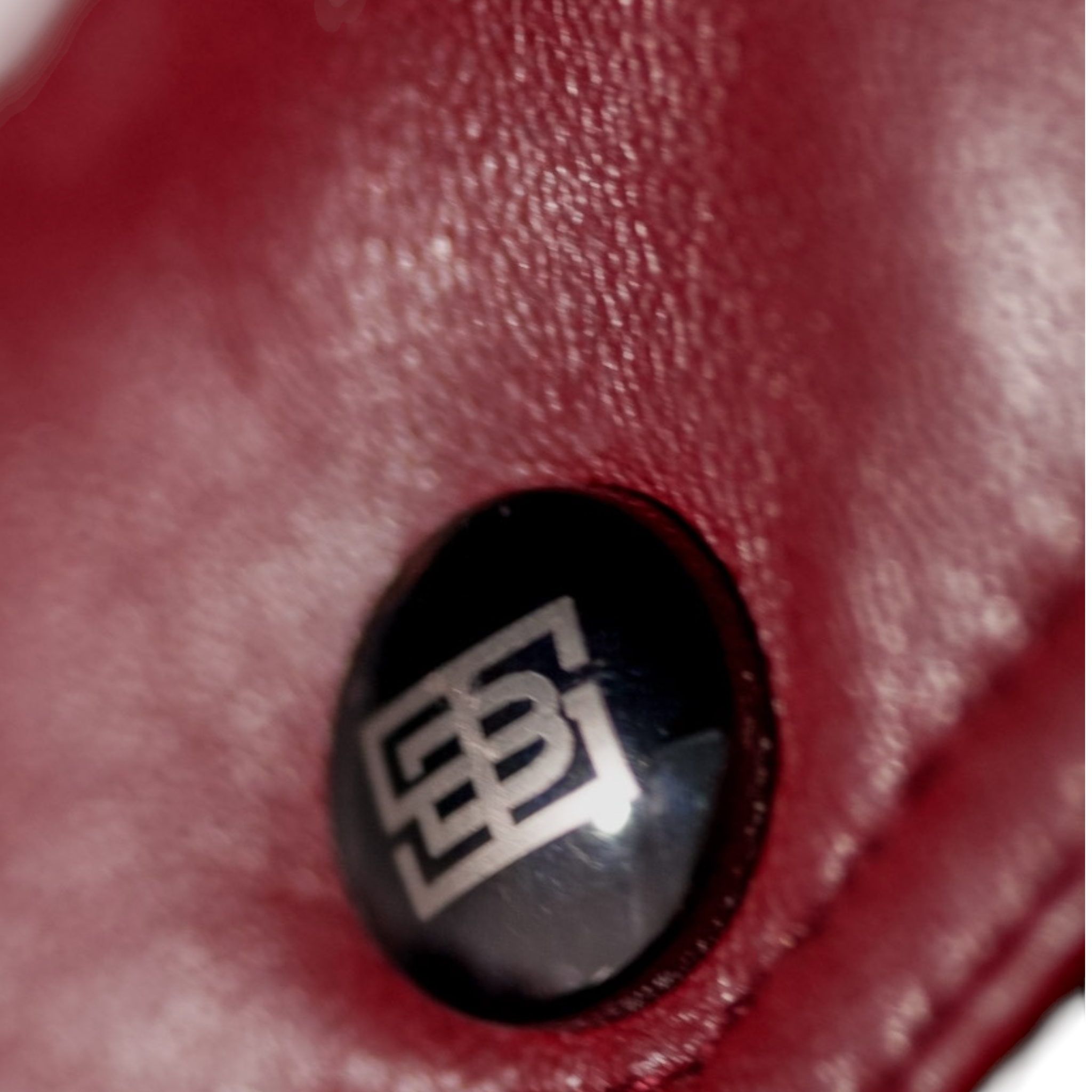 Close-up of a red textured surface with a black circular logo featuring the letter 'B'. Blaatan The Garnet Crimson Edition Crimson Burgundy Leather Jacket for Men