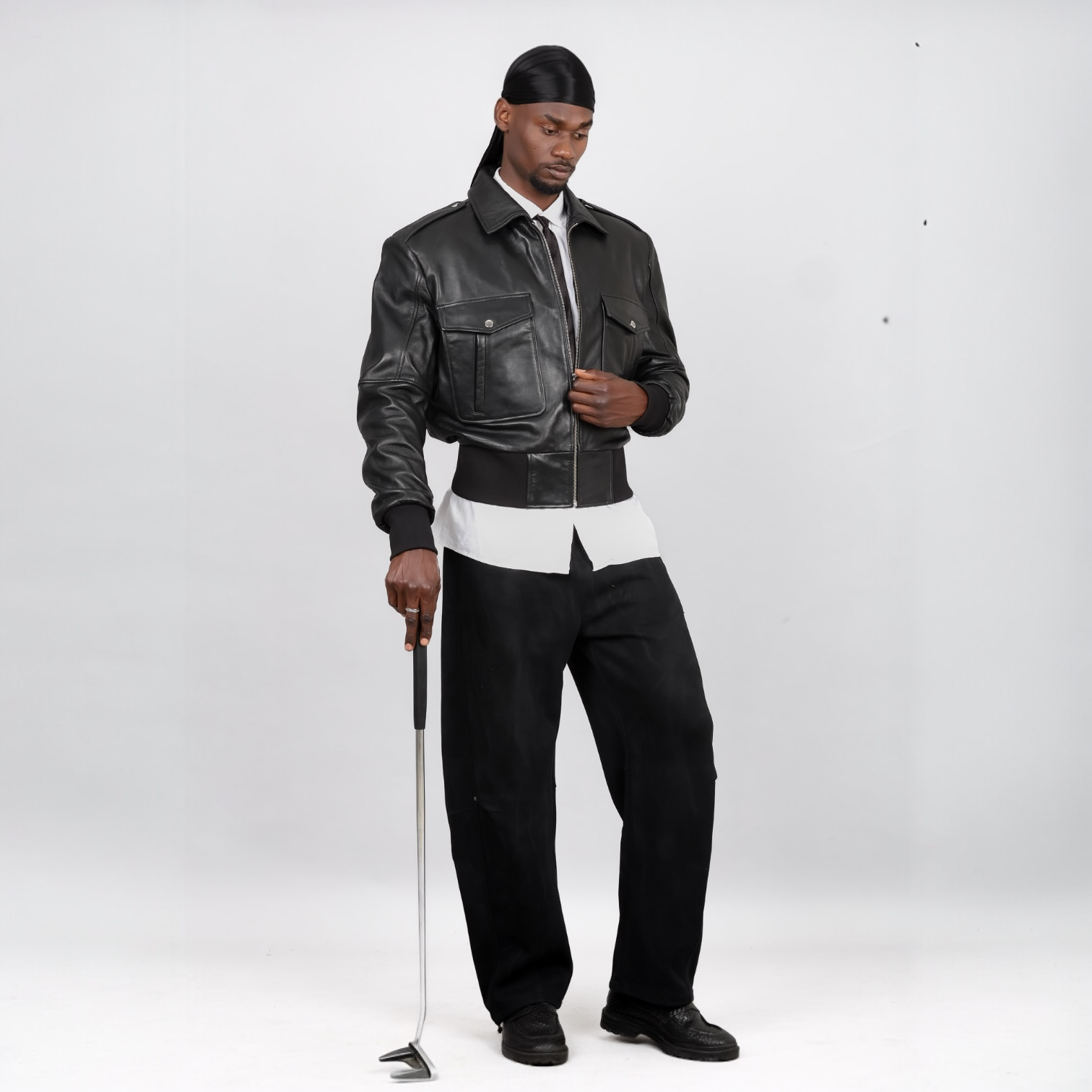 Man wearing a black leather jacket and pants holding a golf club on a white background. Blaatan The Marshal Flight Edition Obsidian Black Aviator Bomber Leather Jacket for Men